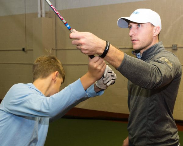 Youth golf coach helping a young junior golfer with grip and stance at an indoor Chicago suburbs facility.